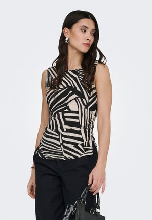Kvinde med langt mørkt hår bærer en sort og beige zebra-stribet ærmeløs top og sorte bukser, og hun holder en sort håndtaske i den ene hånd.