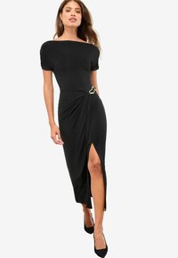 Rochie neagră midi cu mâneci scurte, design cu față răsucită, accesorii din aur și o fante laterală. Fabricată dintr-un material moale și elastic.