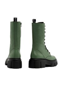 Bottes en cuir vert montant à la cheville, avec une semelle épaisse noire et une fermeture éclair latérale. Comprennent un design à lacets et une boucle à l'arrière pour un enfilage facile.