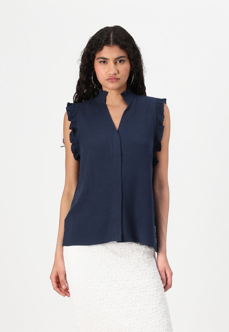 Blusa senza maniche blu navy con scollo a V e spalle arricciate. Realizzata in un tessuto leggero, presenta una leggera lucentezza e una vestibilità morbida.