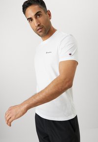 White cotton t-shirt with a crew neckline, short sleeves, and a small navy logo on the chest. Smooth texture, classic style.