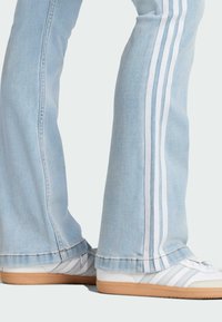 Svetlomodré zvonové džínsy majú biele bočné pruhy, skombinované s bielymi teniskami so šedými akcentmi a gumenou podrážkou. Viditeľné švy na leme.