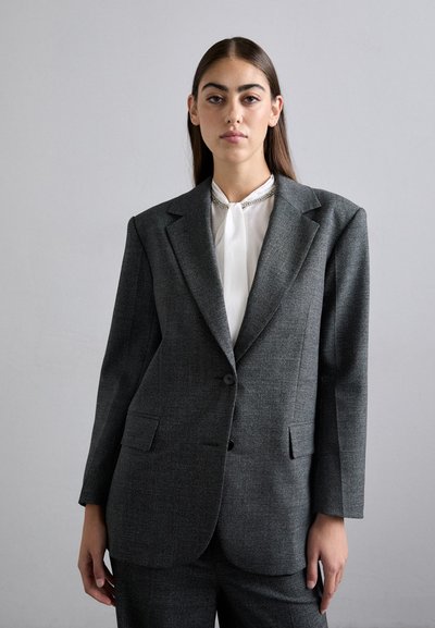 Gray tailored blazer with structured shoulders, single button closure, textured fabric, and two front pockets, paired with a white blouse.