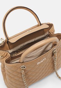 Tan quilted håndtaske med en glat overflade, kædehåndtag i guldfarve og en lynlåslukning i toppen. Indersiden har en lys stofforet og rum.