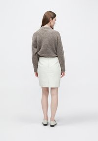 Rjav pulover z teksturo, krem krilo iz usnja do kolen. Mehka tkanina, enostavna zasnova, zadaj razporek, kombinirano s svetlimi čevlji.