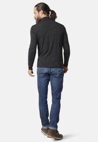 Donkergrijze trui met een hoge kraag, slim fit ontwerp, en geribde manchetten, gedragen met blauwe jeans en bruine veterschoenen. Achteraanzicht.