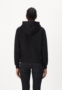 Sweat-shirt à capuche noir présenté de dos, avec des poignets et un ourlet côtelés, en tissu doux et au fit décontracté.