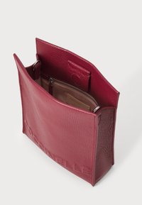 Deep burgundy leather bag with an open top, featuring a logo embossed on the front. Interior has a zippered pocket and soft lining.