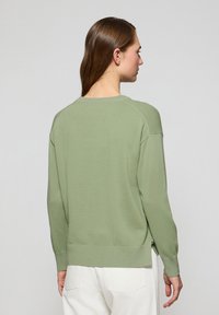 Grön långärmad tröja med rundad halsringning, ribbade ärmslut och nederkant, samt sprund på sidorna. Slät textur med avslappnad passform.