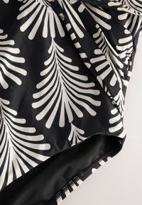 Tissu noir et blanc avec un motif abstrait en forme d'éventail, montrant un détail froncé et le bord d'une couture d'un vêtement.