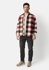 Rød og creme ternet flannel skjorte med knaplukning og brystlomme, båret over en beige top, kombineret med sort jeans og beige sneakers.