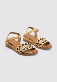 Sandales jaunes à lanières avec une tige tissée ornée d'accents noirs et bronzés, une semelle plate et une bride de cheville réglable.