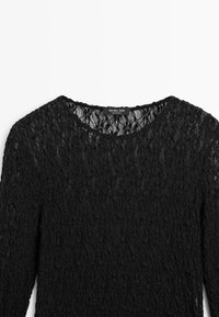 Top in pizzo nero a maniche lunghe con scollo rotondo, caratterizzato da un motivo floreale, una finitura testurizzata e un'etichetta di marca sul collo.
