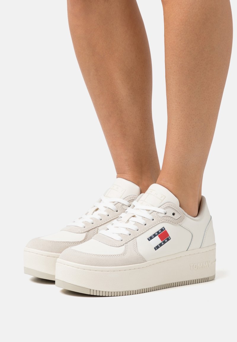 Vita plattformssneakers i mjukt mocka och läder, med en färgglad logotypapplikation på sidan. Platt gummisula med texturerat grepp.