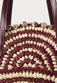 Πλεκτή τσάντα χειρός από μανταρίνι και κρέμα από ψάθα με κυκλικό σχέδιο, διαθέτοντας υφασμάτινες λεπτομέρειες και δερμάτινες λαβές.