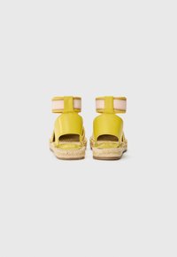 Sandali espadrille in pelle gialla con retro aperto, cinturini elasticizzati bicolore alla caviglia e suola in juta intrecciata. Finitura liscia e lucida.