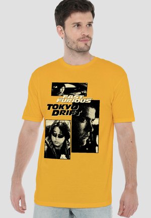 Mann trägt gelbes T-Shirt mit schwarz-weißen Filmstills und Text vom Film Fast and the Furious: Tokyo Drift auf der Vorderseite.