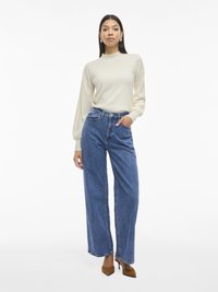 Cream high-neck sweater with long sleeves, paired with high-waisted, wide-leg blue denim jeans. Brown pointed-toe heels accent the outfit.