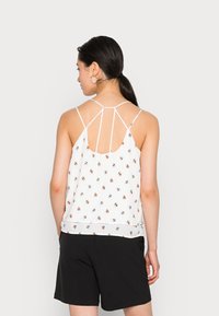 Top de alças finas com padrão floral branco, apresentando um design de costas fendida. Combinado com calções pretos, exibindo um ajuste descontraído.