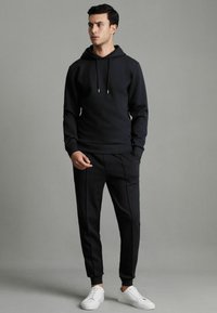 Hanorac negru cu șnur, asortat cu pantaloni negri tapered cu cusături laterale, completat cu adidași albi. Material neted.