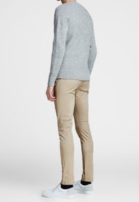 Suéter de punto gris con cuello redondo, combinado con pantalones beige de corte ajustado y zapatillas blancas, visto desde la parte de atrás.