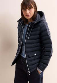 Giacca puffa blu navy con zip frontale, cappuccio regolabile con stringa e polsini elasticizzati. Presenta un'imbottitura orizzontale e una tasca frontale con chiusura a scatto.