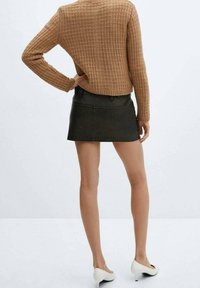 Brązowy sweter o teksturowym wzorze z długimi rękawami, w połączeniu z ciemnozieloną spódnicą dżinsową. Białe buty na wysokim obcasie dopełniają stylizację.