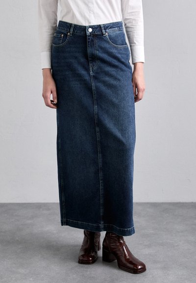 Mørkeblå denim maxi nederdel med lige snit, der har forlommer og knaplukning. Bæres med glinsende brune hæle boots.