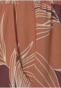 Getextureerde stof in roestkleur met witte botanische print; met gevouwen secties en elastische details langs de taille, wat een gelaagd ontwerp benadrukt.