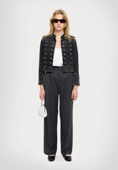 Sort denim cropped jakke med metalknapper, parret med grå højtaljede bukser og en lille hvid håndtaske. Sorte firkantede solbriller.