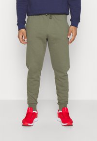 Grüne Jogginghose aus weichem Baumwollmix, mit einem elastischen Bund und Kordelzug sowie einem schmal geschnittenen Bein. Kombiniert mit roten Sneakern.
