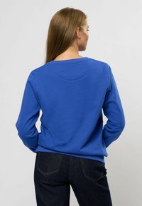 Felpa blu con scollo rotondo e maniche lunghe. Presenta un tessuto testurizzato e una vestibilità casual, abbinata a jeans scuri.