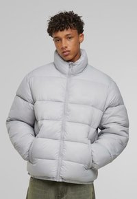 Jachetă puffer gri deschis, cu guler înalt, design capitonat, fermoar frontal și buzunare laterale, confecționată dintr-un material neted.