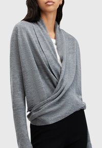 Szary kardigan z miękką fakturą, z przodu układający się w kopertę, z prążkowanymi mankietami i luźnym krojem. Noszony na białej bluzce.