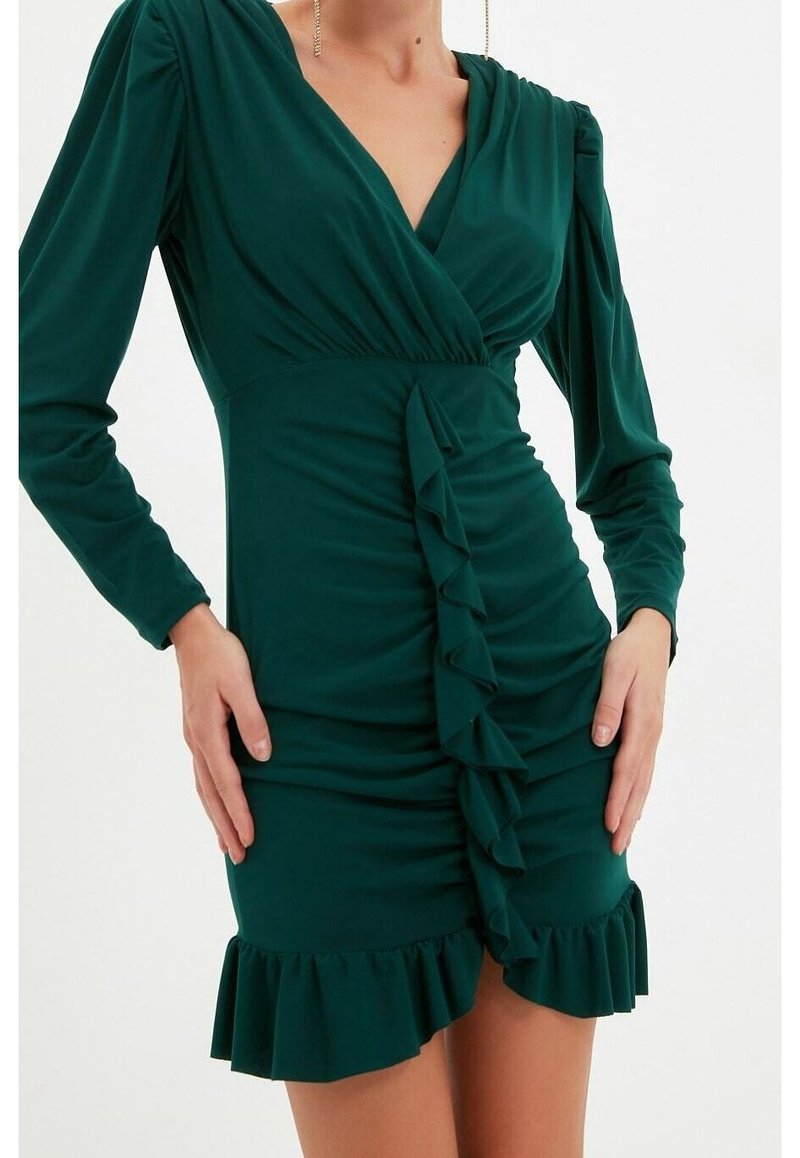 Robe verte à manches longues en tissu doux. Présente un design croisé, un devant froncé avec des volants verticaux et un ourlet froncé.