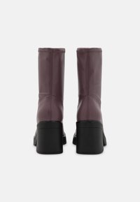 Botas de color ciruela hasta la rodilla con una textura brillante, diseño ajustado y tacones gruesos negros. Costuras decorativas recorren las costuras.