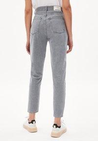 Harmaat korkeavyötäröiset farkut kapenevilla lahkeilla, takataskuilla ja brändätyllä vyötärönauhalla, yhdistettynä valkoisiin lenkkareihin, joissa on mustat yksityiskohdat.