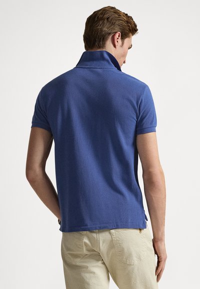 Collared blue polo shirt made of textured fabric, featuring short sleeves and side slits, paired with light-colored pants.