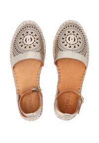 Metalické zlaté espadrilky mají složité vykrojené květinové vzory, hnědou koženou podšívku a uzavřenou špičku s nastavovacími řemínky kolem kotníku.