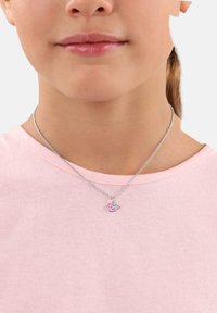 Collana in argento con un ciondolo a forma di uccello rosa con dettagli neri, indossata da una persona con una maglietta rosa chiaro.