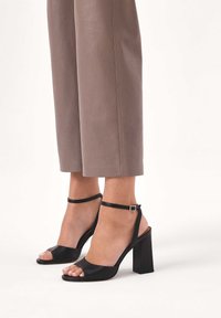 Mustat korkokengät avoimella varvassuunnittelulla, sileää nahkamateriaalia, nilkkaremmi soljella ja neliskulmaisella paksulla korolla.