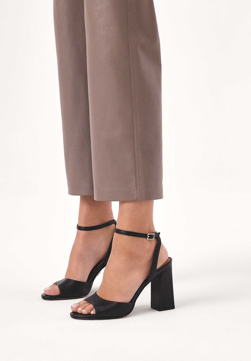 Mustat korkokengät avoimella varvassuunnittelulla, sileää nahkamateriaalia, nilkkaremmi soljella ja neliskulmaisella paksulla korolla.