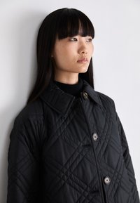 Μαύρο επενδυμένο μπουφάν με μεγάλο γιακά, με διαγώνιες ραφές, κουμπιά από κέρατο και υφή στον ύφασμα.