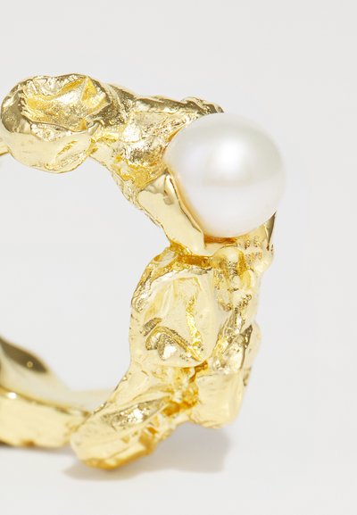Gold-textured ring featuring an irregular design with a prominent white pearl. The surface displays varying reflections and highlights.