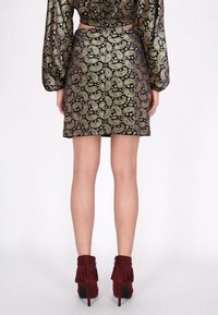 Fustă scurtă, ajustată, din material negru cu un model paisley auriu. Acoperită de botine vișinii, cu detalii din ciuf și toc înalt.