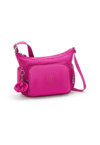 Pink nylon shoulder bag with a curved design, zip pocket, and a fur charm attached. Features adjustable strap and logo patch.