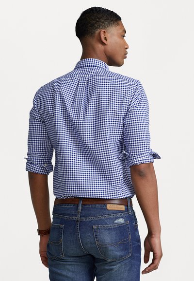 Blue and white gingham check button-up shirt with rolled sleeves, paired with dark denim jeans and a brown leather belt.