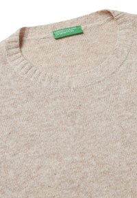 Beżowy sweter robiony na drutach z prążkowanym dekoltem i fakturą. Posiada zieloną metkę z napisem "UNITED COLORS OF BENETTON". Miękki, casualowy design.