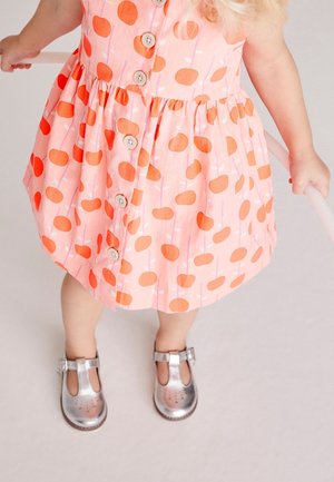 Vestido rosa con lunares naranjas, con botones en la parte delantera y falda fruncida. Zapatos plateados con recortes y detalle de hebilla. Tela suave y ligera.