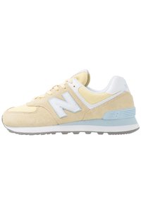 New Balance sneakers med blødt gult ruskind og mesh-overdel, hvide detaljer, en lyseblå logo og en grå gummiydersål.